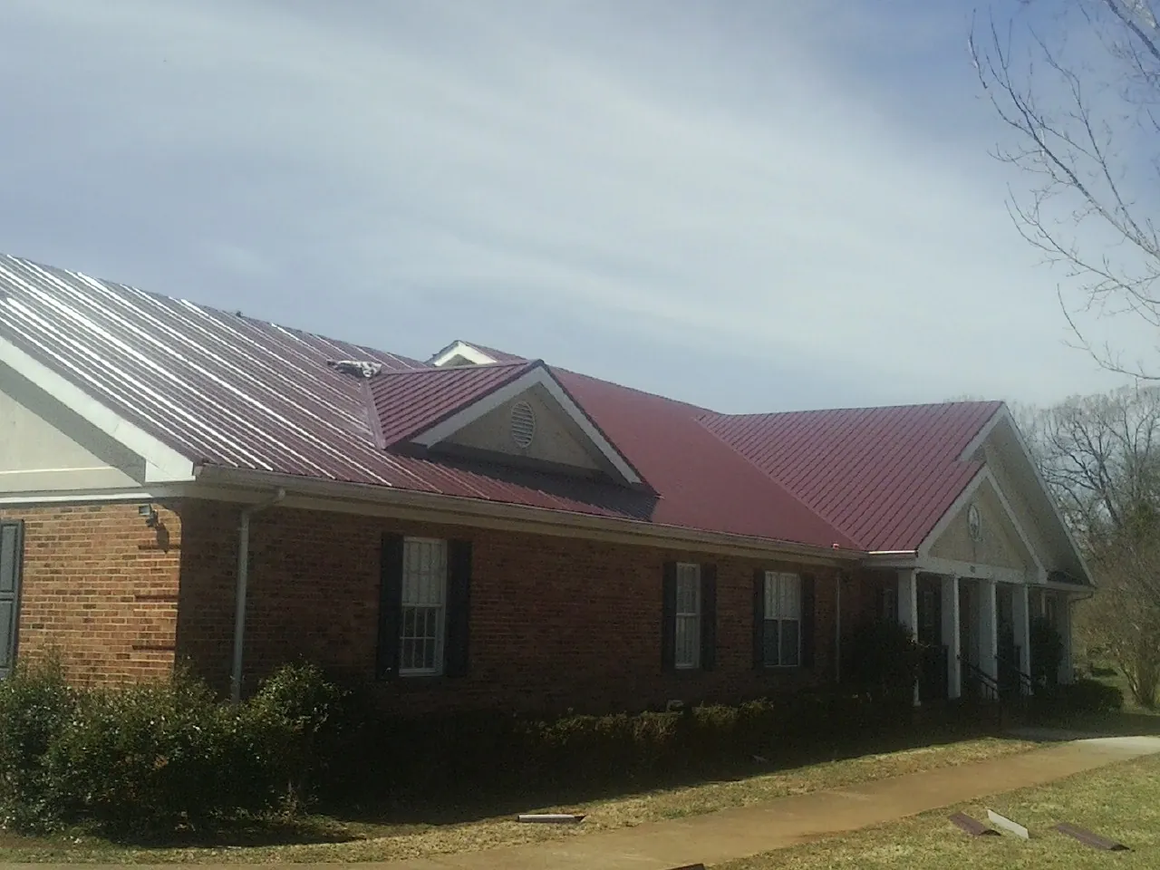 Red metal roof with gabled entries on a long brick building, from a Hail Damage Roof Repair job in Marshallville