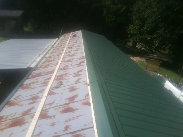 Old rusted panels beside newly installed green metal roofing — Wind Damage Roof Repair by Roofing Brothers in Marshallville