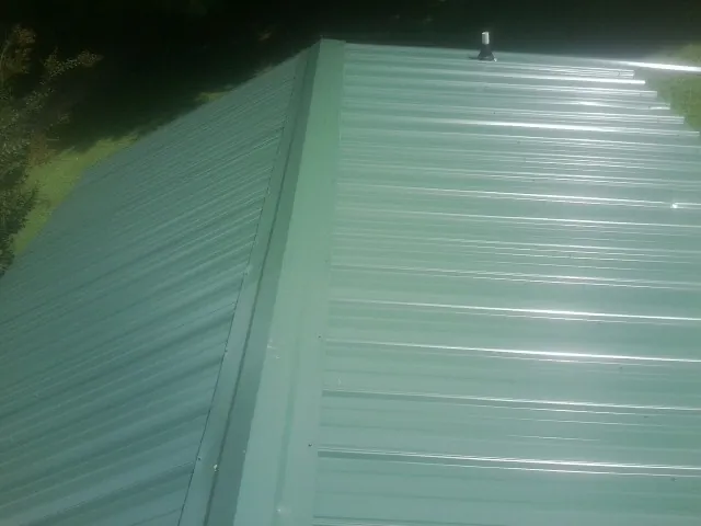 New green metal panels meeting at the ridge of a roof — Flat Roof Repair work by our crew in Marshallville