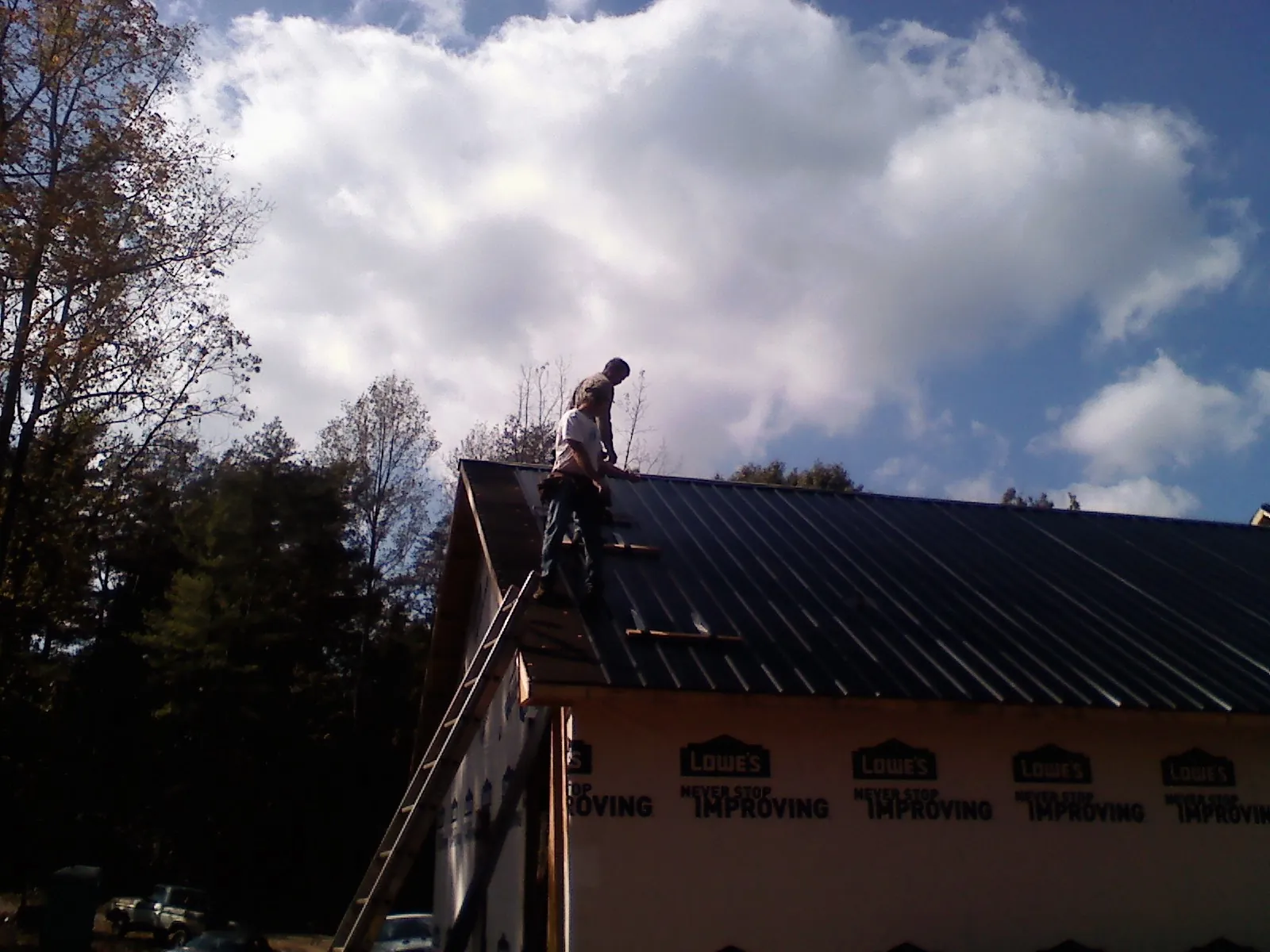 Roofer fastening dark metal panels high against a cloudy sky, from a Roof Inspection job in Marshallville
