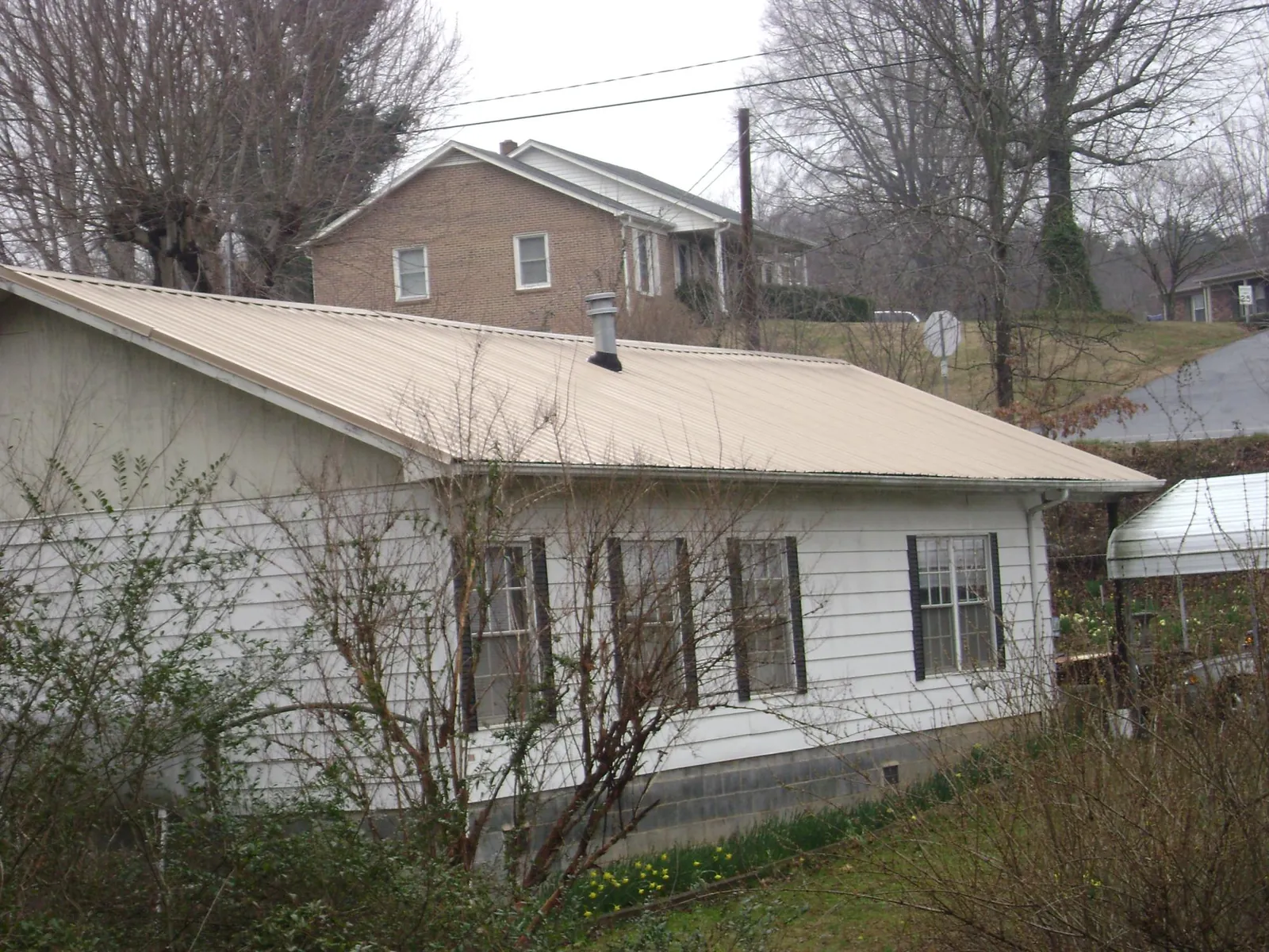 Tan metal roof on a white sided house set into a hillside — Commercial Roofing by Roofing Brothers in Marshallville