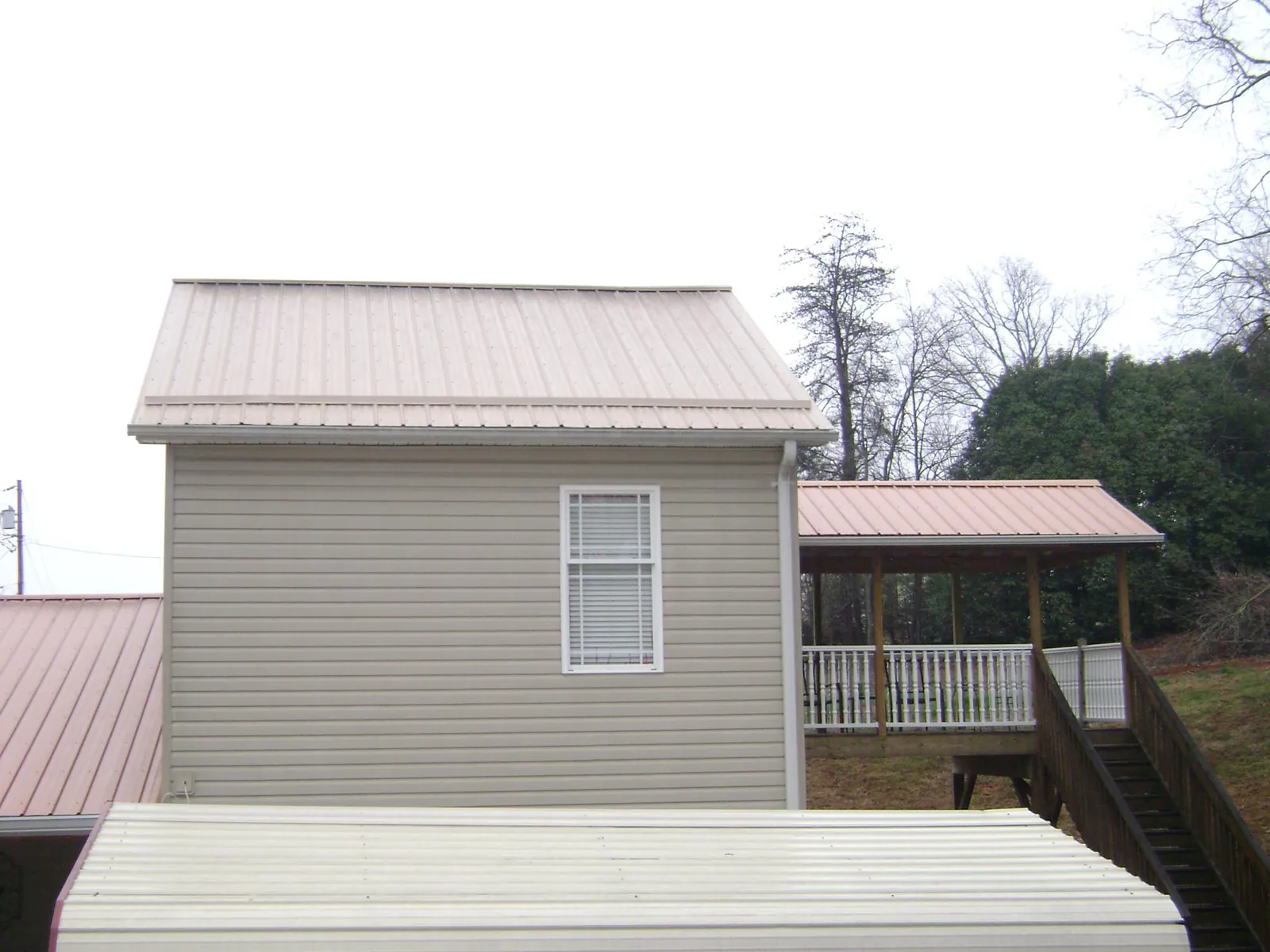 Tan metal roofs on a two story addition and attached porch, from a Roof Replacement job in Marshallville